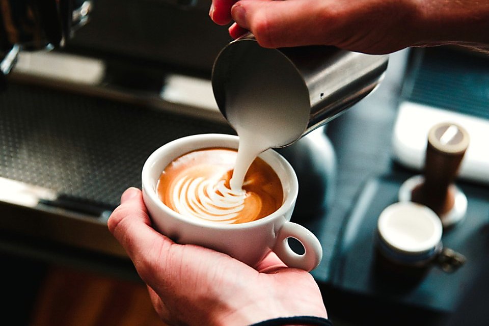 Barista pouring a flat white over a timber counter