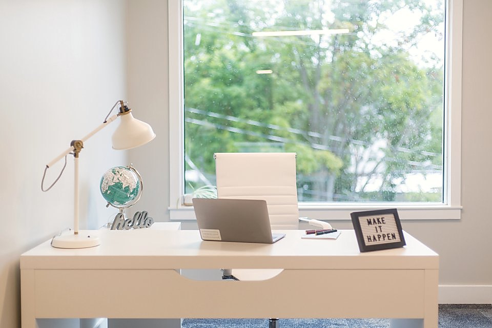 A simple timber desk by a window with a laptop, lamp and plant
