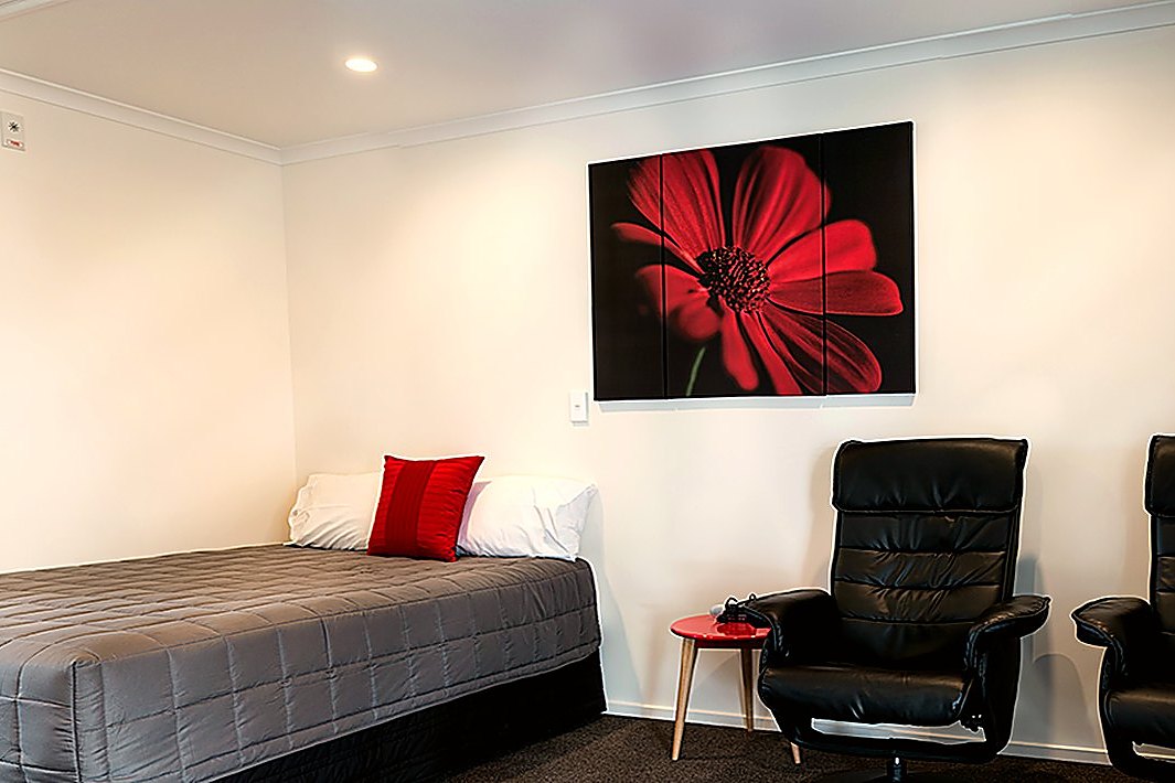 A refurbished studio room with recliner chairs, a made bed and a 32-inch television