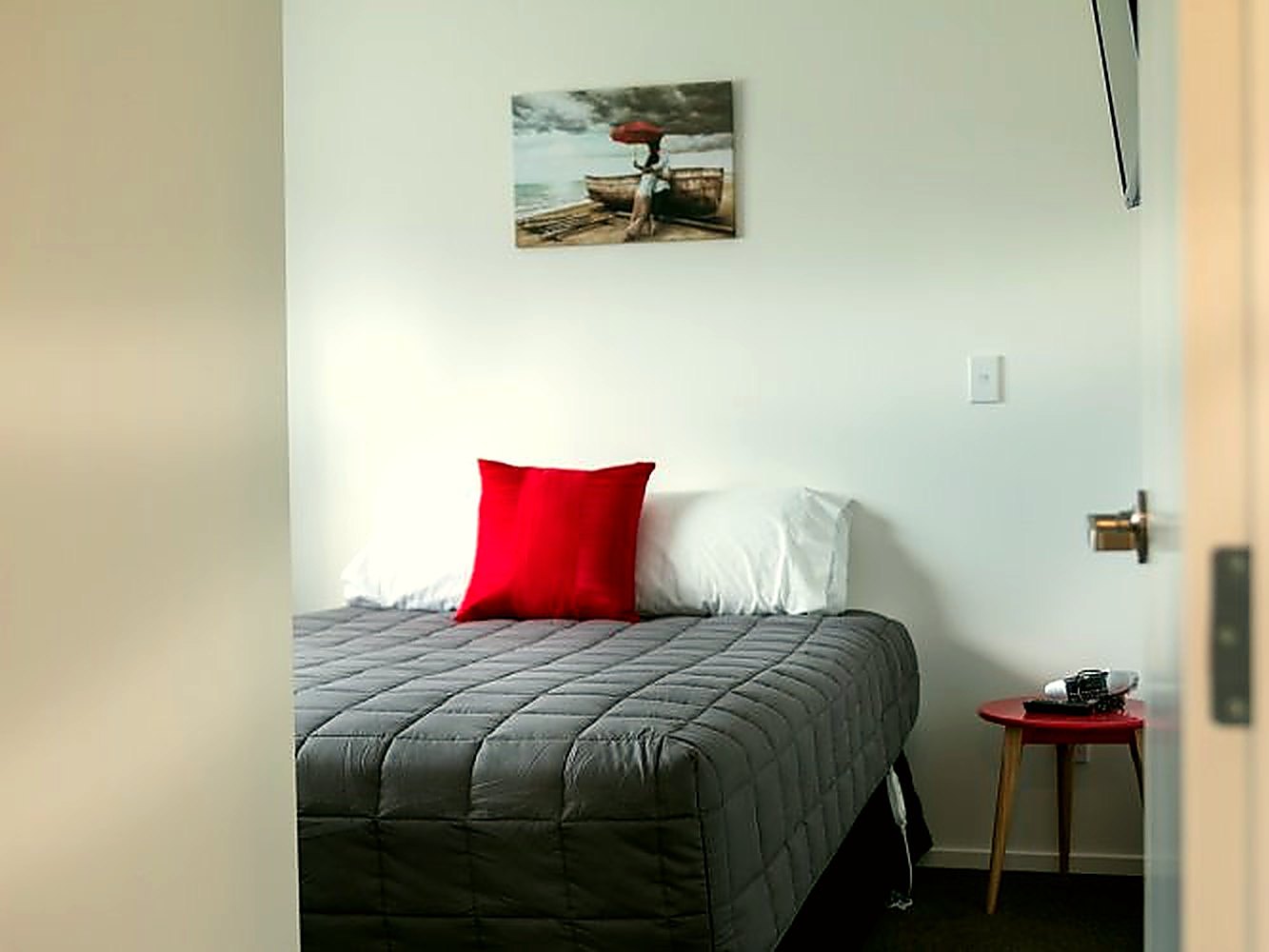 Refurbished studio with a queen bed and red accent cushion