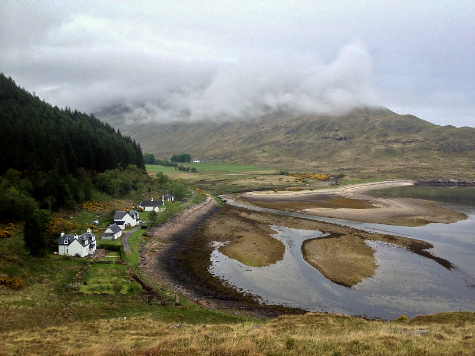 A rural estuary with low green hills and a winding road
